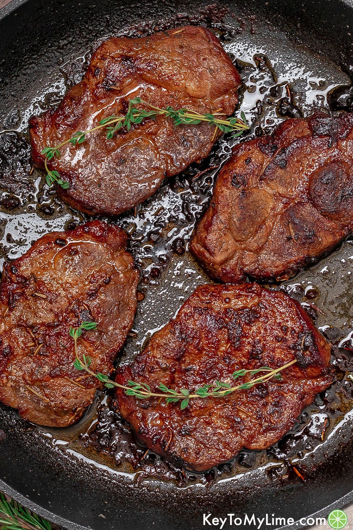 An overhead image of glistening pork steaks ready to be served in a large cast iron skillet.