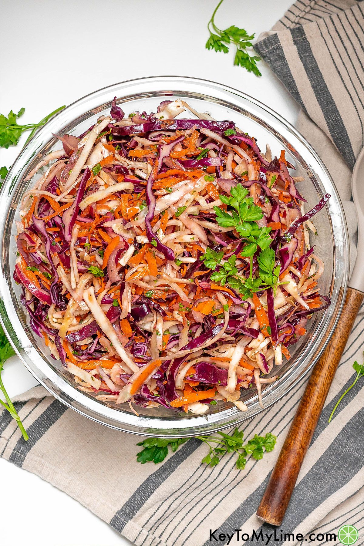 A freshly made vinegar coleslaw garnished with parsley in a large glass bowl.