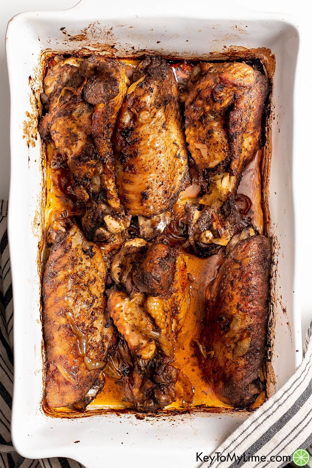 A single layer of crispy turkey wings in a large casserole dish with a striped napkin to the side.