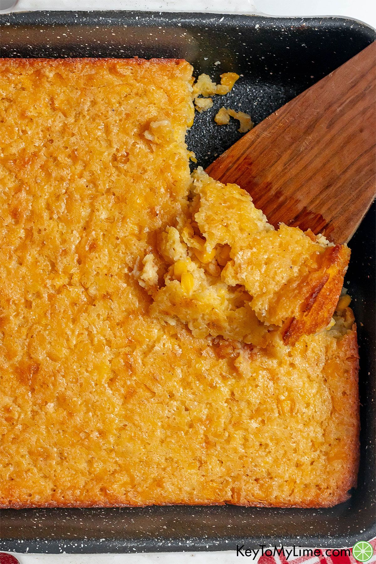An overhead image of corn casserole dish scooping out a serving with a wooden spatula.
