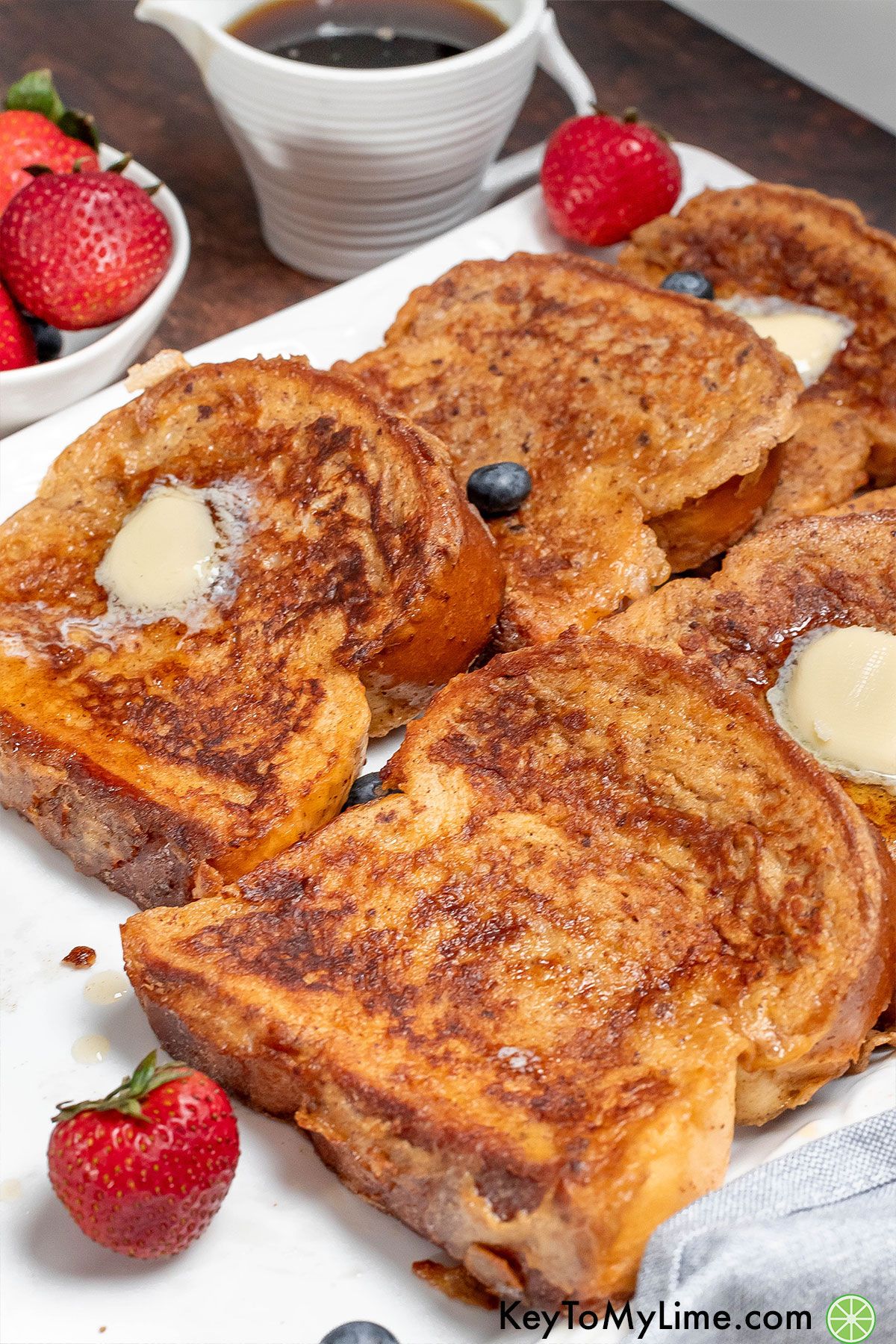 A side image of multiple slices of freshly made French toast garnished with strawberries on a white plate.