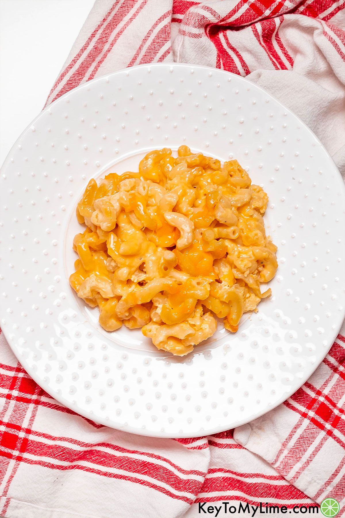 An overhead image of a serving of Patti Labelle's mac and cheese on a white plate on top of a striped napkin.