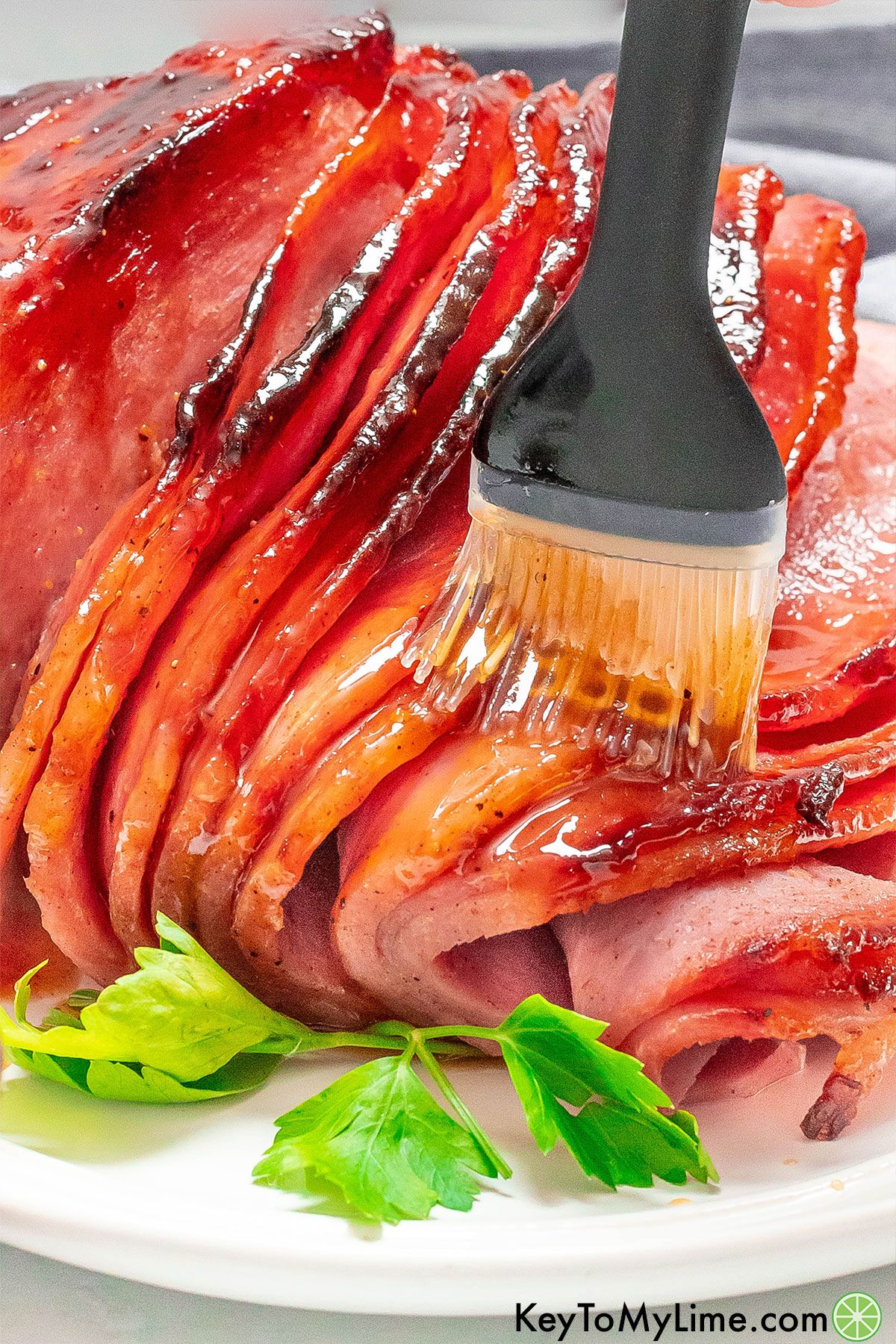 Basting a cooked air fryer ham with ham glaze.