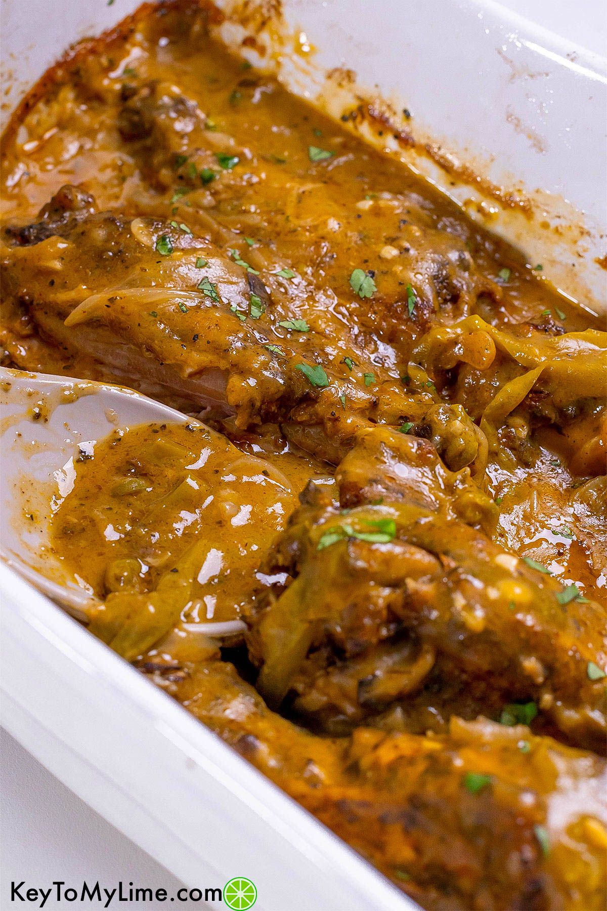 A close up image of a casserole dish with turkey wings and a serving spoon resting inside.