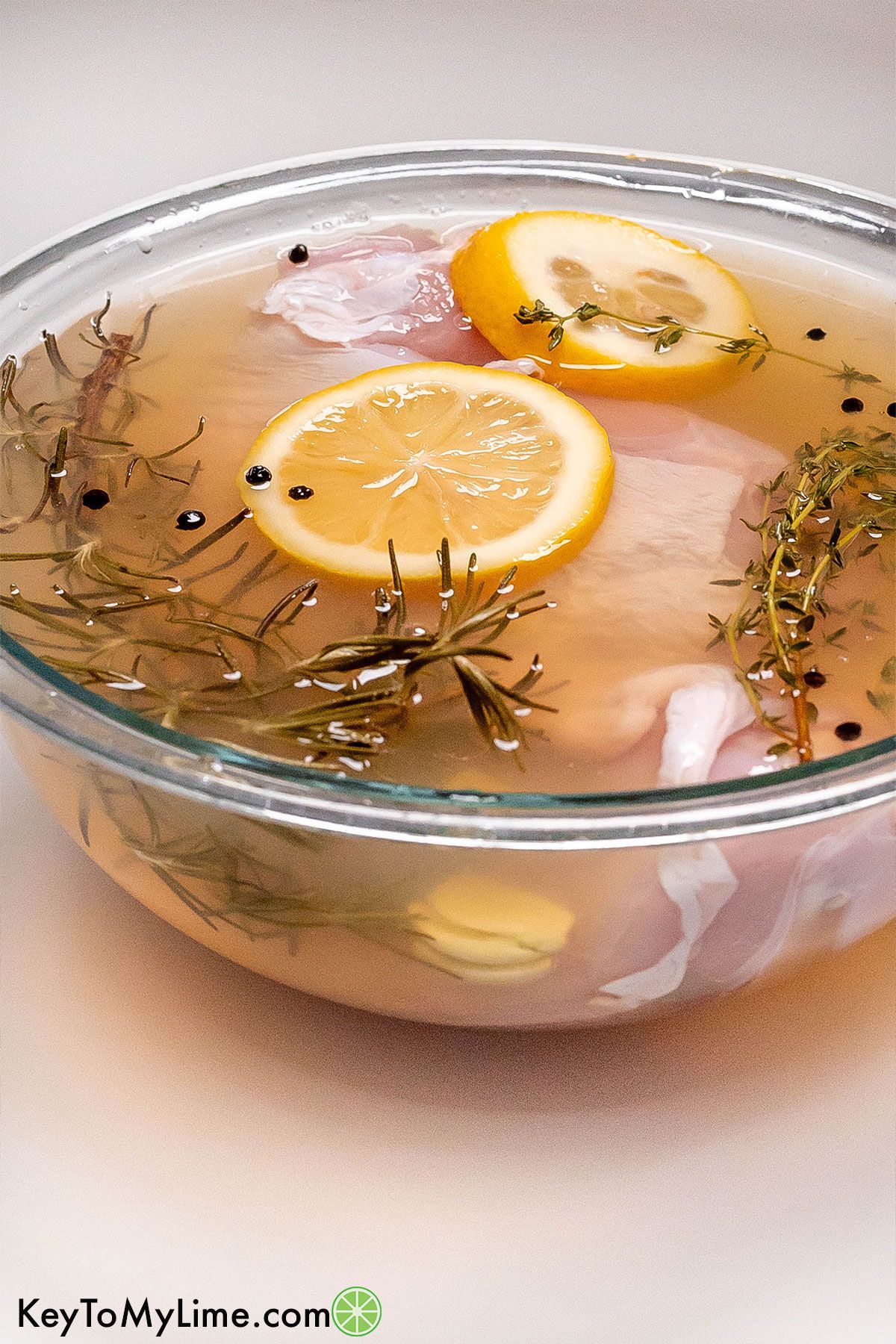 A large bowl of brine with a turkey breast submerged and herbs throughout.