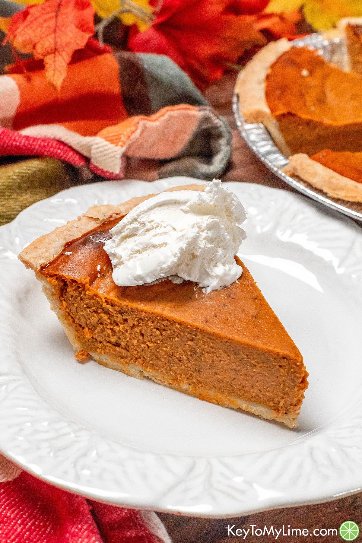 A slice of pie on a plate with fall decorations in the background.