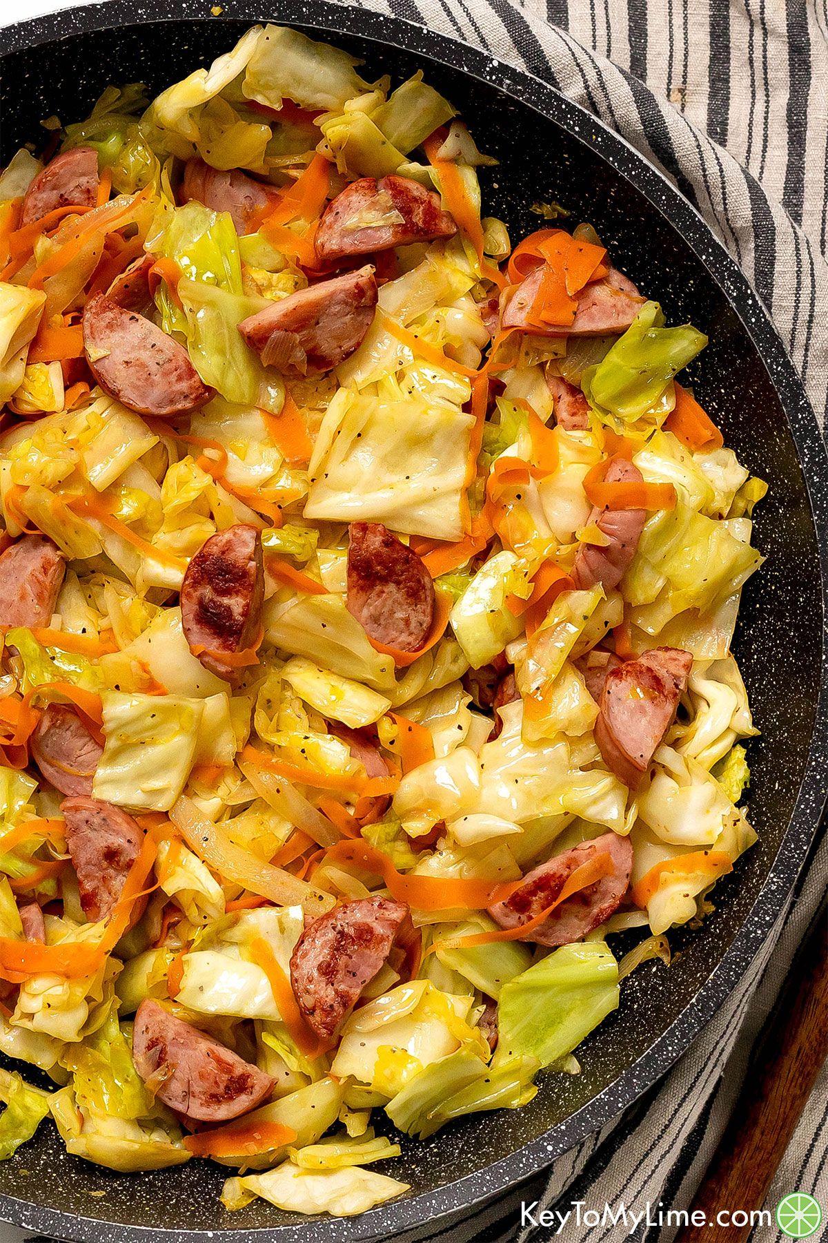 An overhead image of fried cabbage and sausage in a skillet over a napkin.