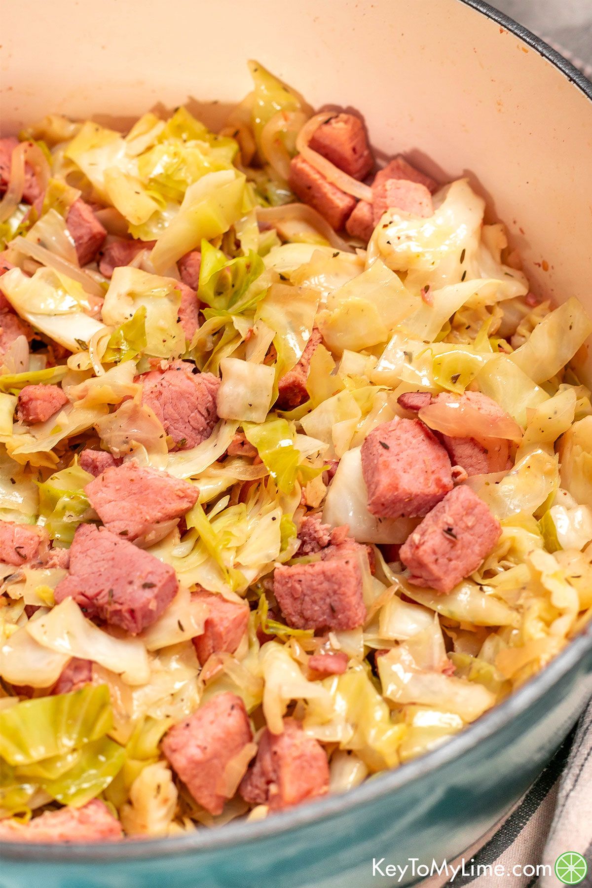 A close up of a large dutch oven full of cooked cabbage with ham throughout.